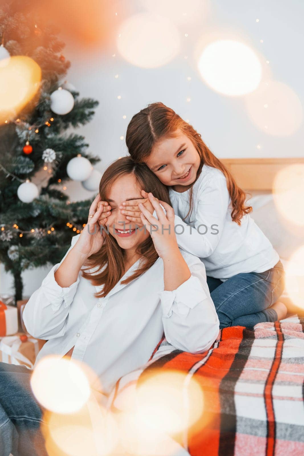 Mother with her little daughter is having fun indoors on the bed.