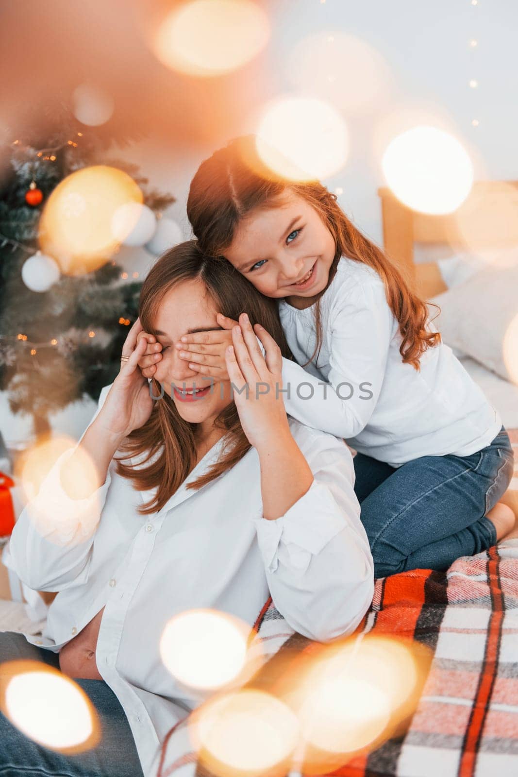 Mother with her little daughter is having fun indoors on the bed.