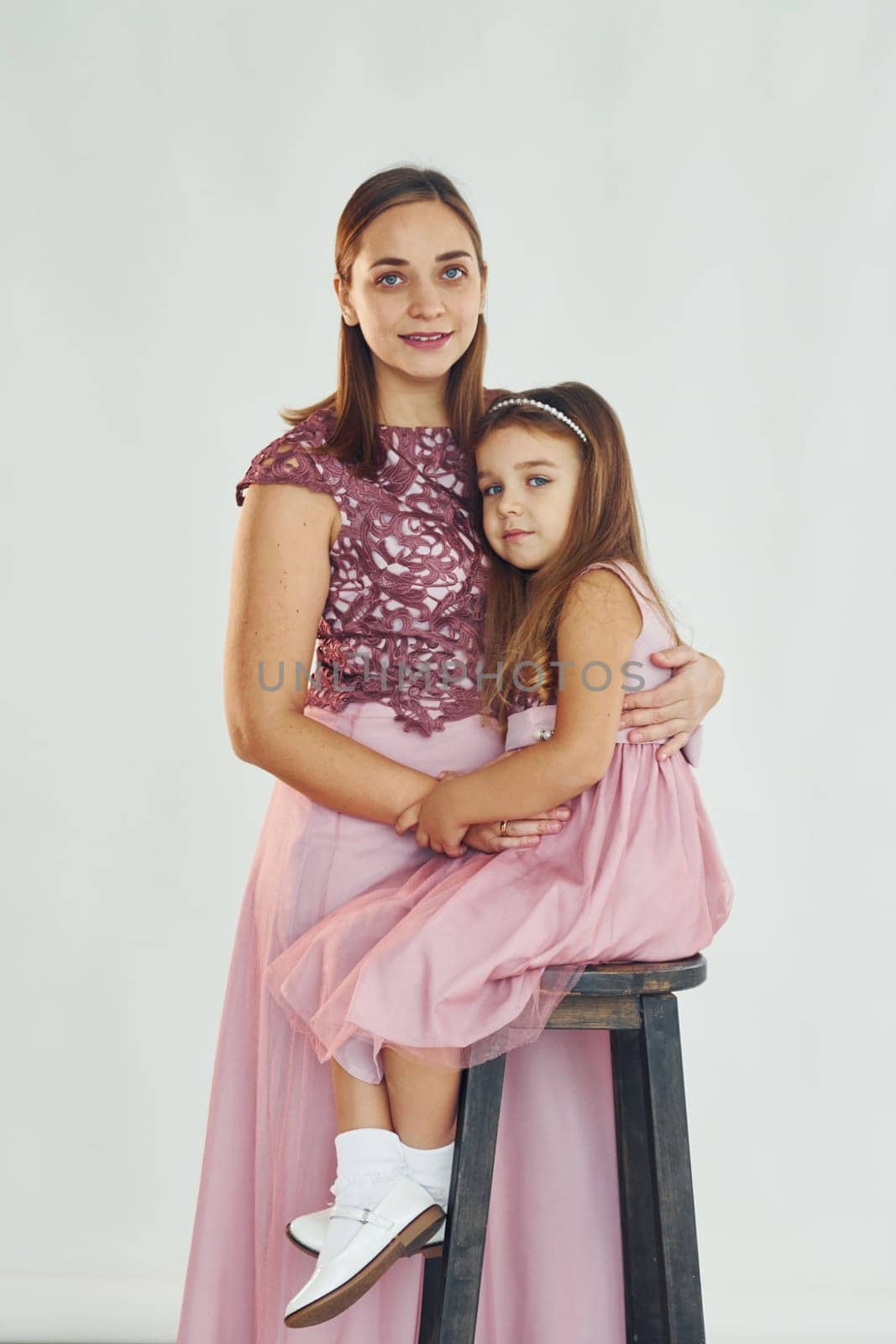 Woman in dress standing with her daughter in the studio with white background.