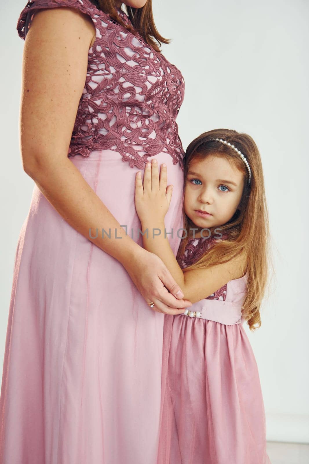 Conception of anticipation. Pregnant mother. Woman in dress standing with her daughter in the studio with white background.