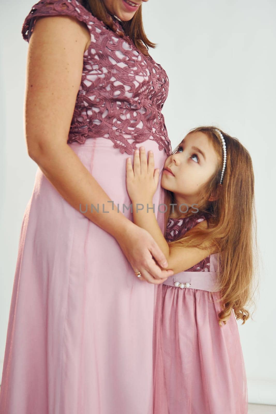 Conception of anticipation. Pregnant mother. Woman in dress standing with her daughter in the studio with white background.