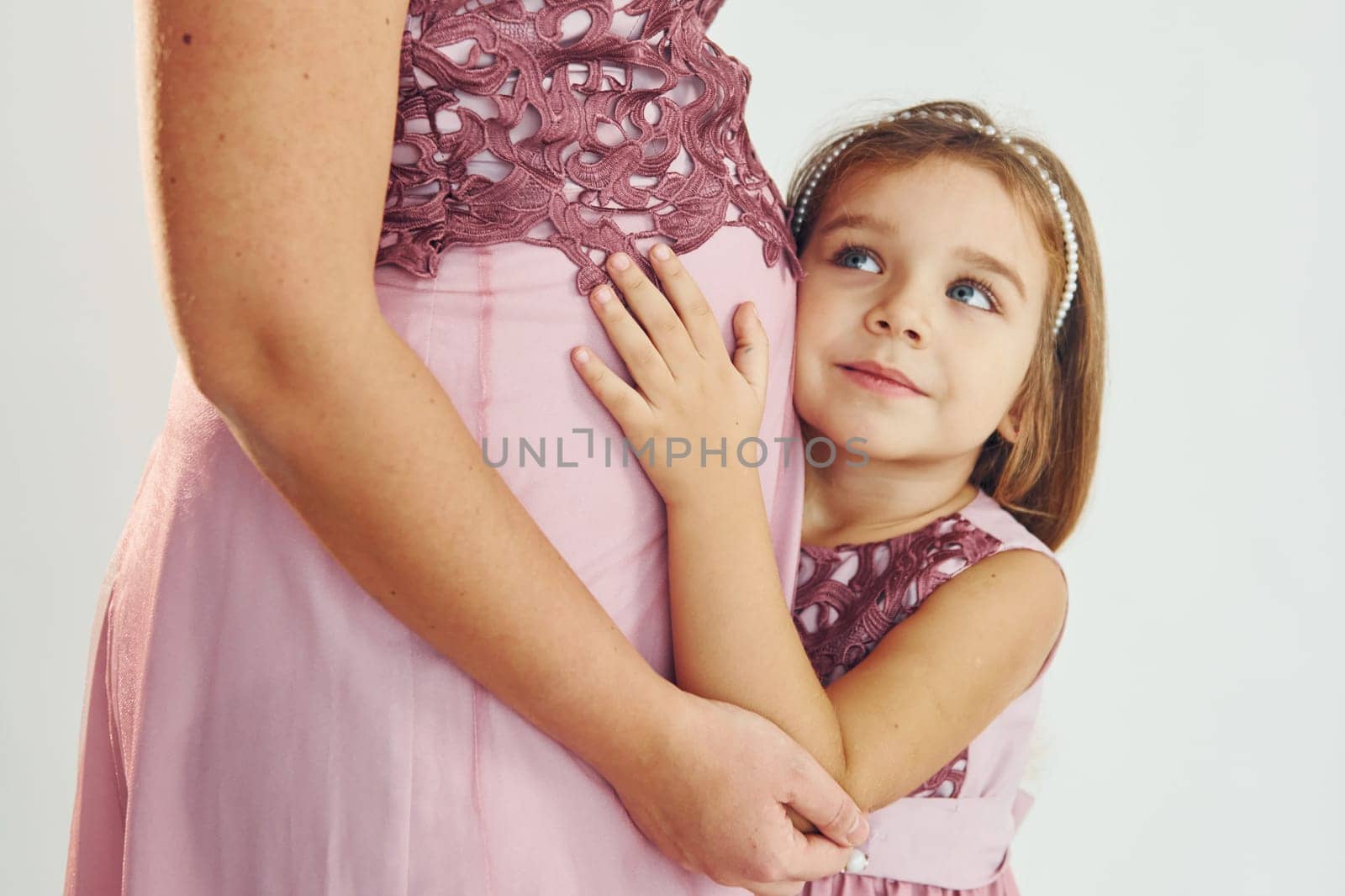 Woman is pregnant. Mother in dress standing with her daughter in the studio with white background.