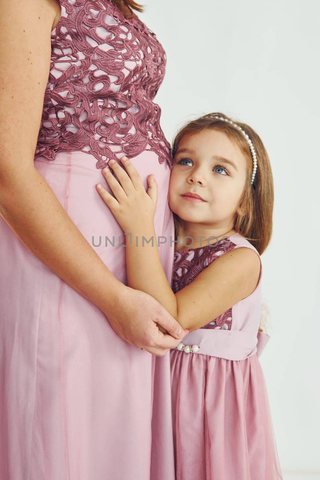 Conception of anticipation. Pregnant mother. Woman in dress standing with her daughter in the studio with white background.