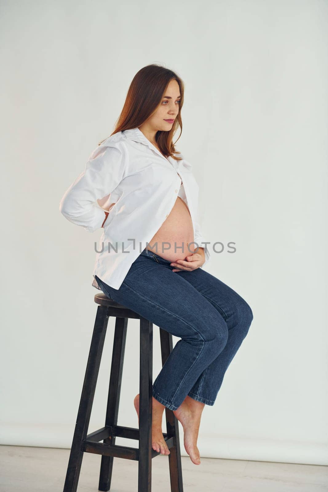 Pregnant woman is sitting on the chair in the studio.