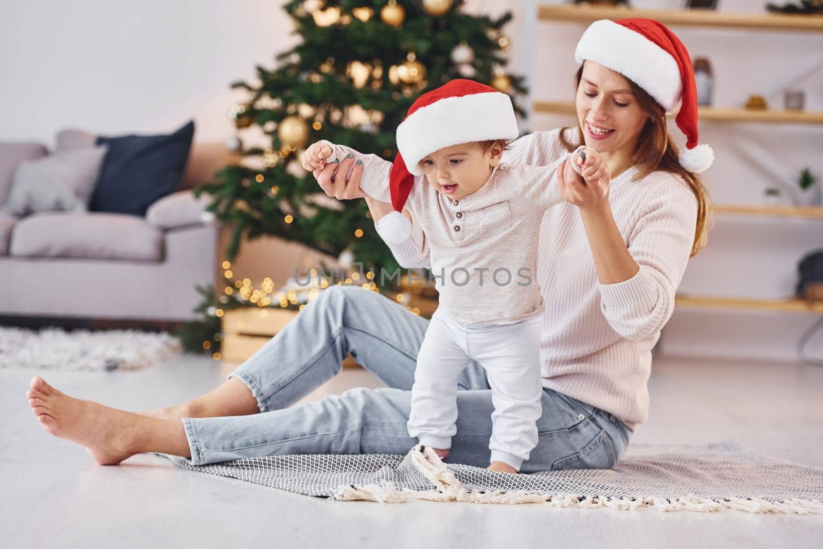 In Santa hats. Mother with her little daughter is indoors at home together.