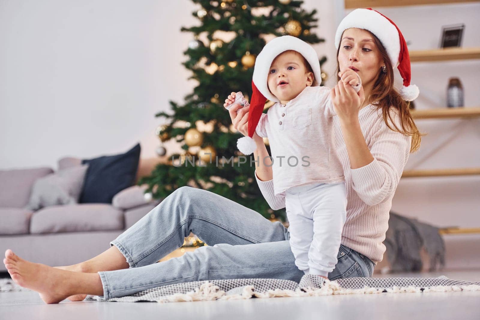 In Santa hats. Mother with her little daughter is indoors at home together.