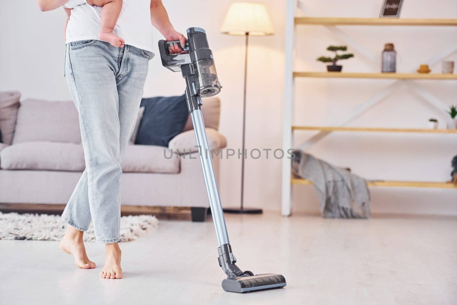 Using of the vacuum cleaner. Mother with her little daughter is indoors at home together.