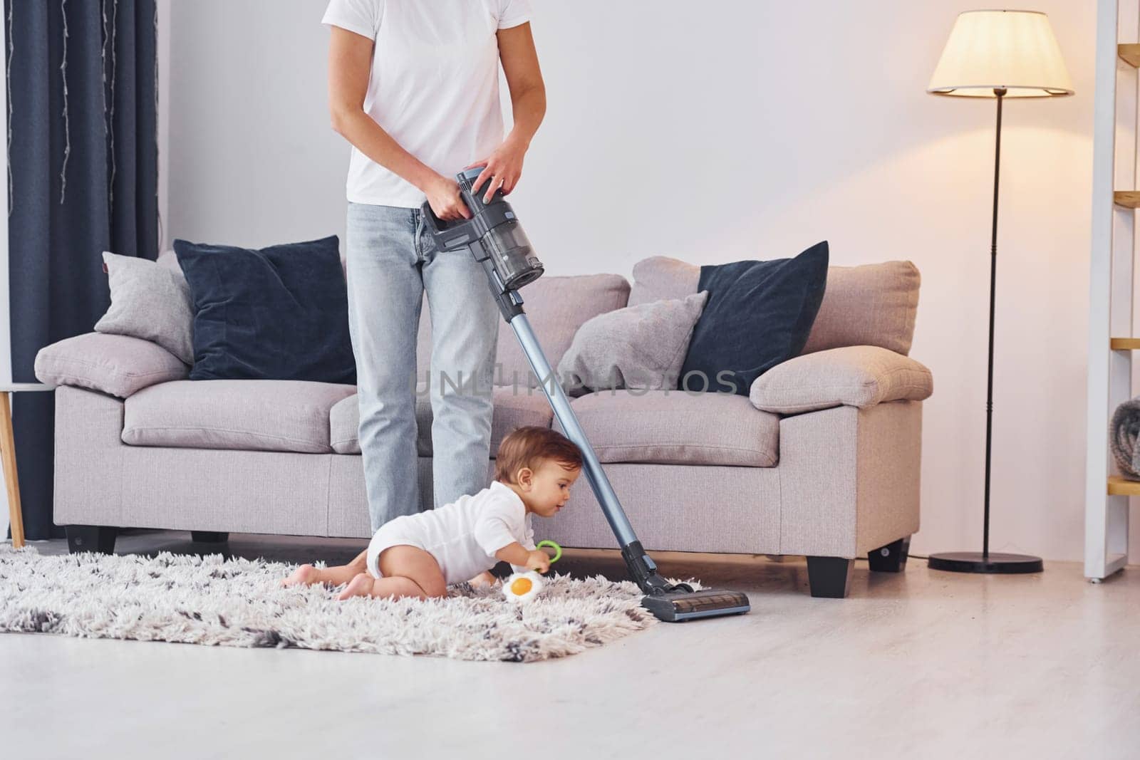 Using of the vacuum cleaner. Mother with her little daughter is indoors at home together.