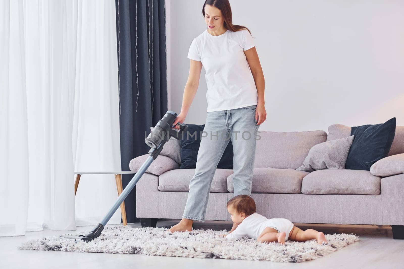 Using of the vacuum cleaner. Mother with her little daughter is indoors at home together.