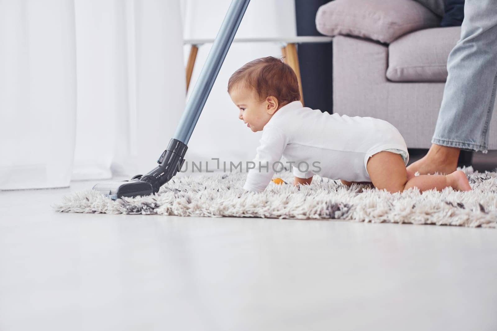 Using of the vacuum cleaner. Mother with her little daughter is indoors at home together.