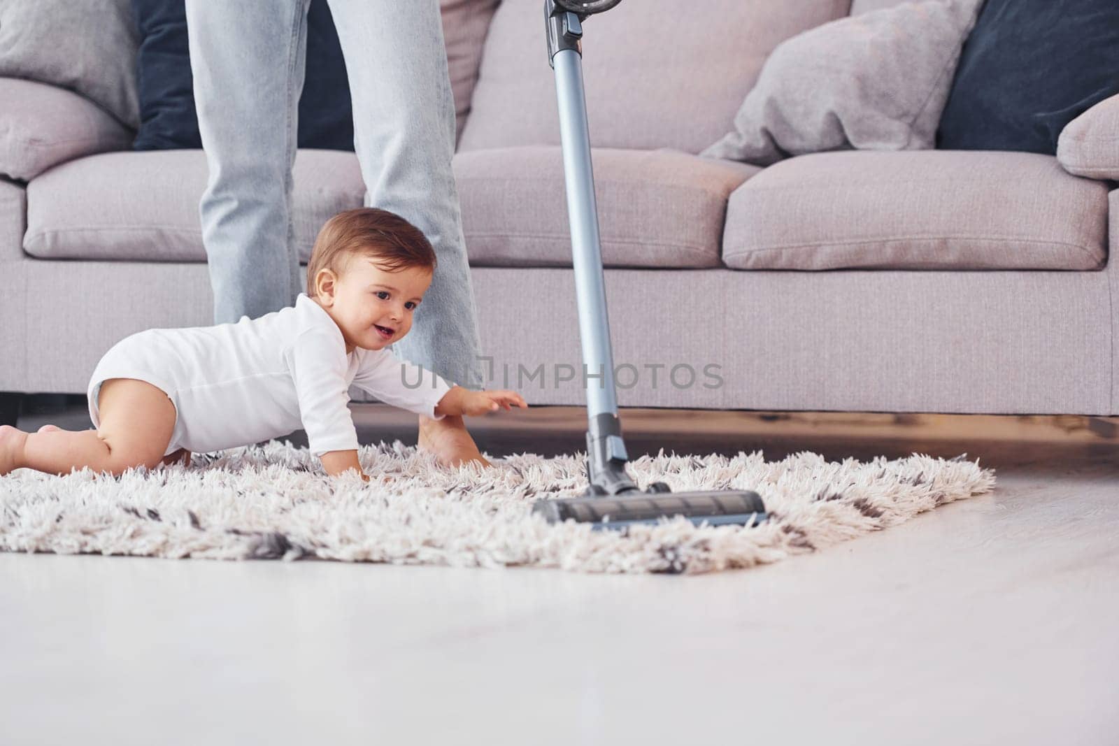 Using of the vacuum cleaner. Mother with her little daughter is indoors at home together.