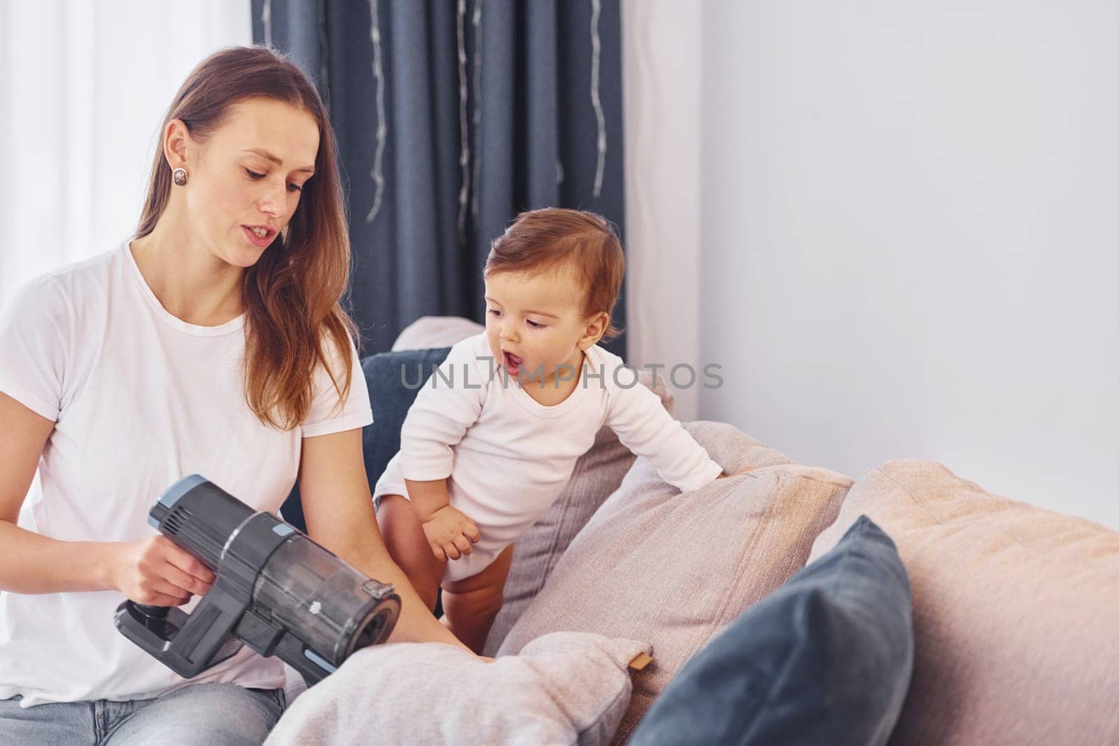 Sitting on the bed with vacuum cleaner part. Mother with her little daughter is indoors at home together.