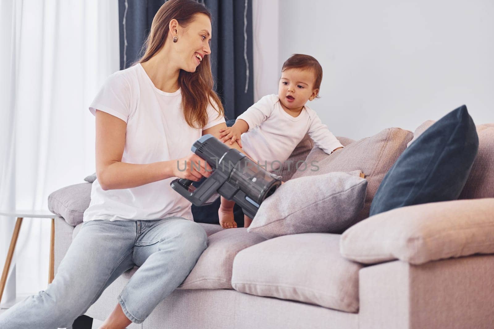 Sitting on the bed with vacuum cleaner part. Mother with her little daughter is indoors at home together.