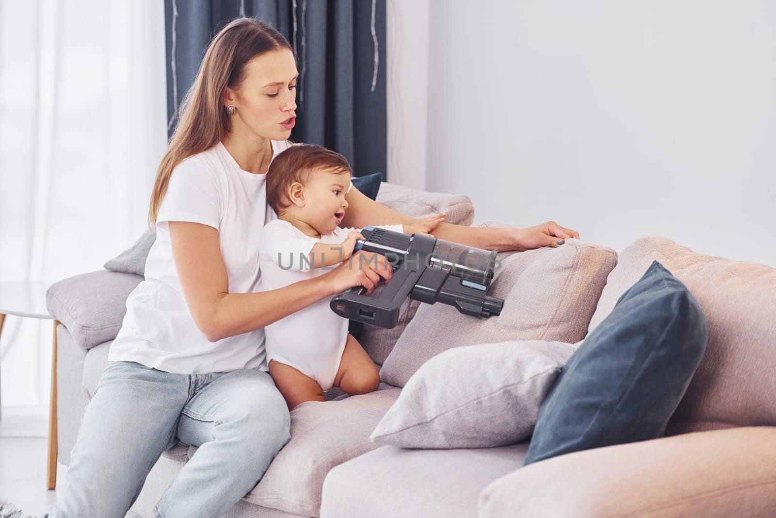 Sitting on the bed with vacuum cleaner part. Mother with her little daughter is indoors at home together.