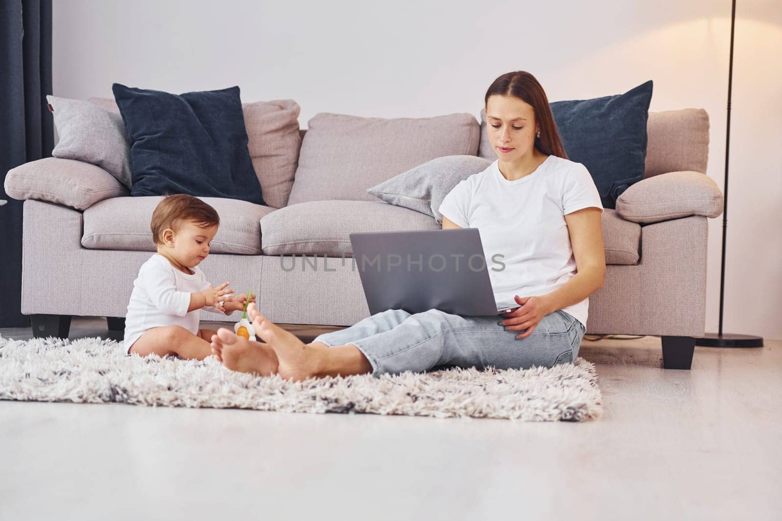 Woman working by using laptop. Mother with her little daughter is indoors at home together.