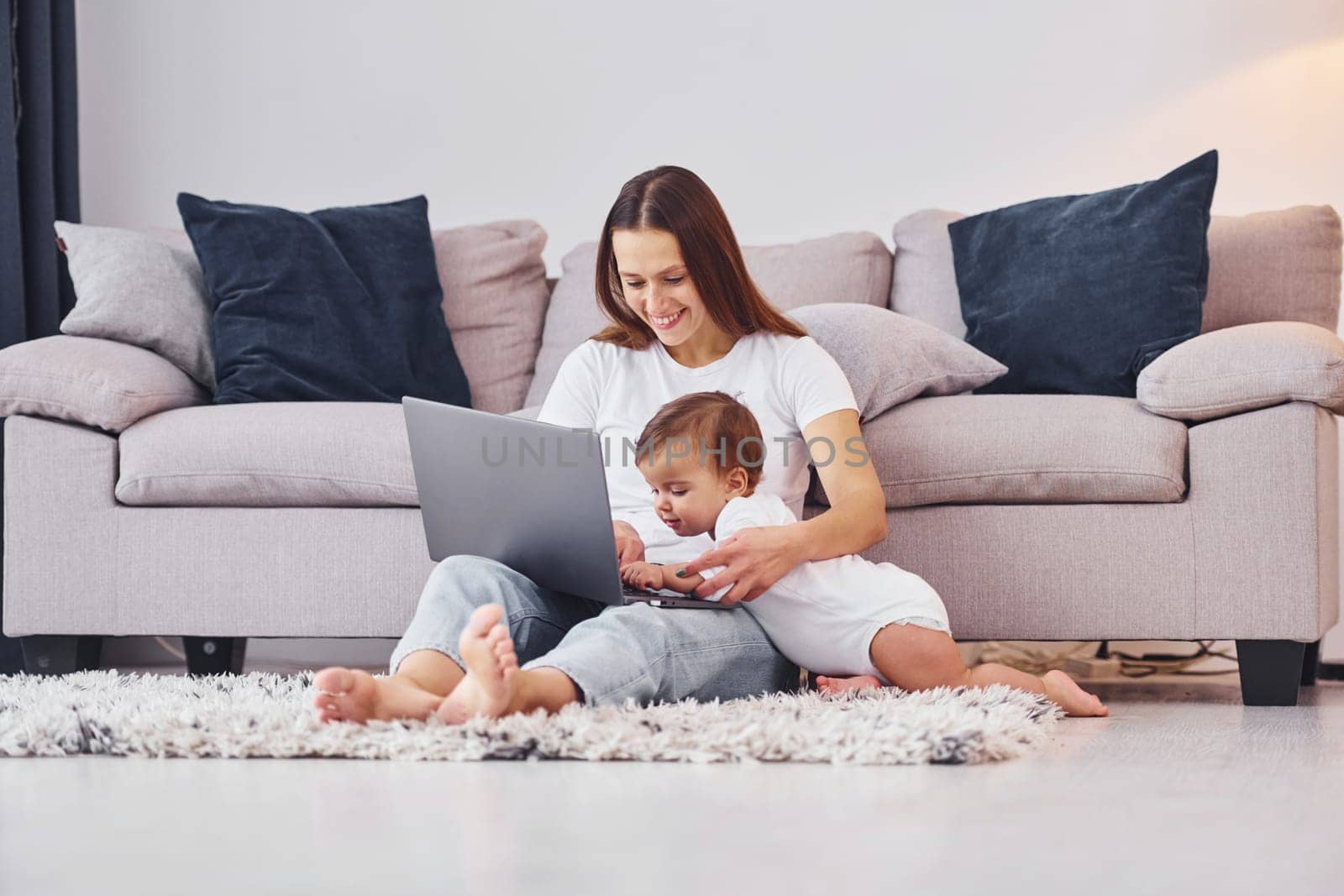 Using laptop. Mother with her little daughter is indoors at home together.