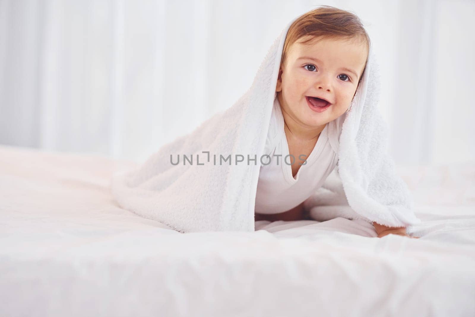 With white towel. Cute little baby is indoors in the domestic room.
