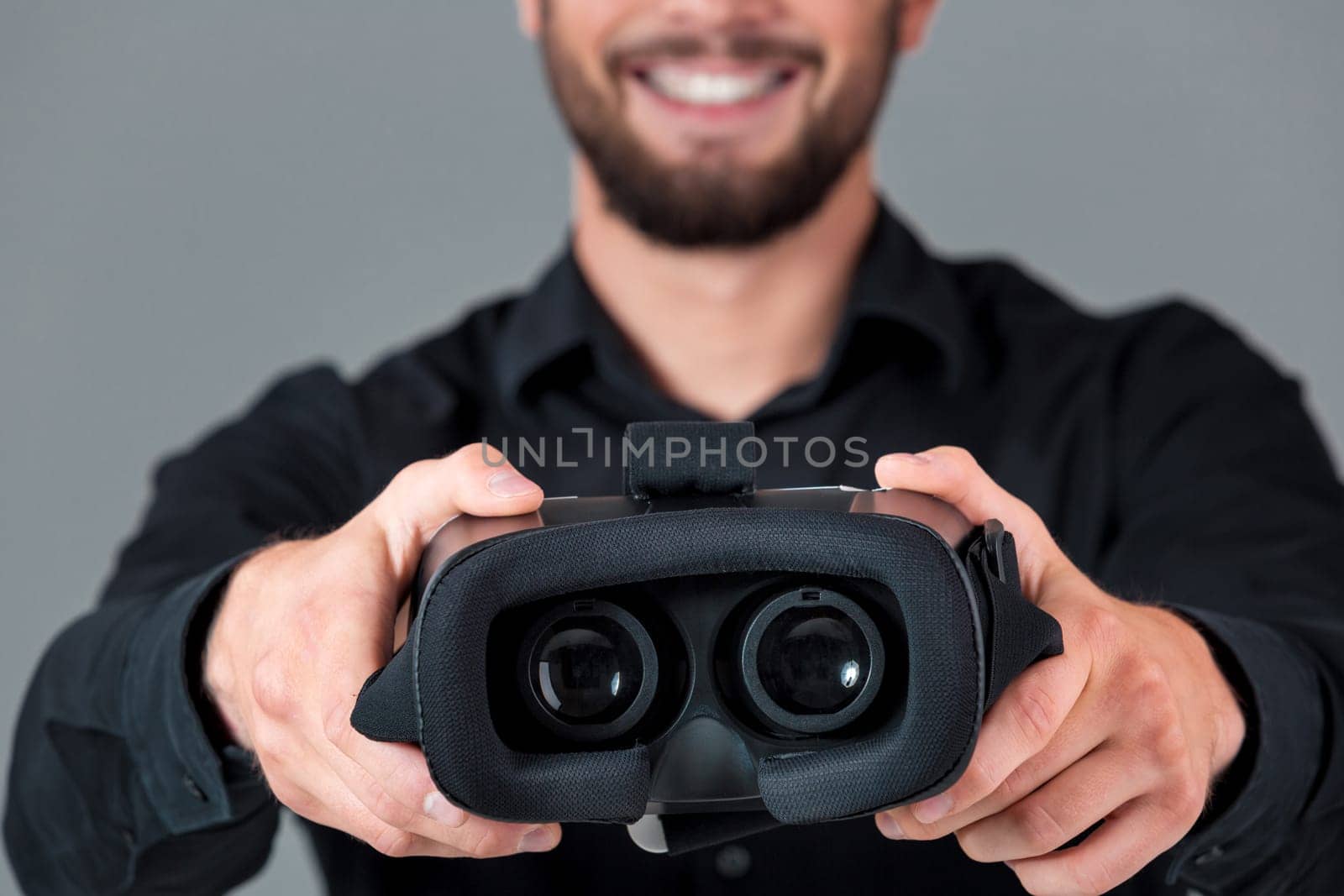 Excited young man using a VR headset and experiencing virtual reality on grey blue background. He holds glasses for viewer