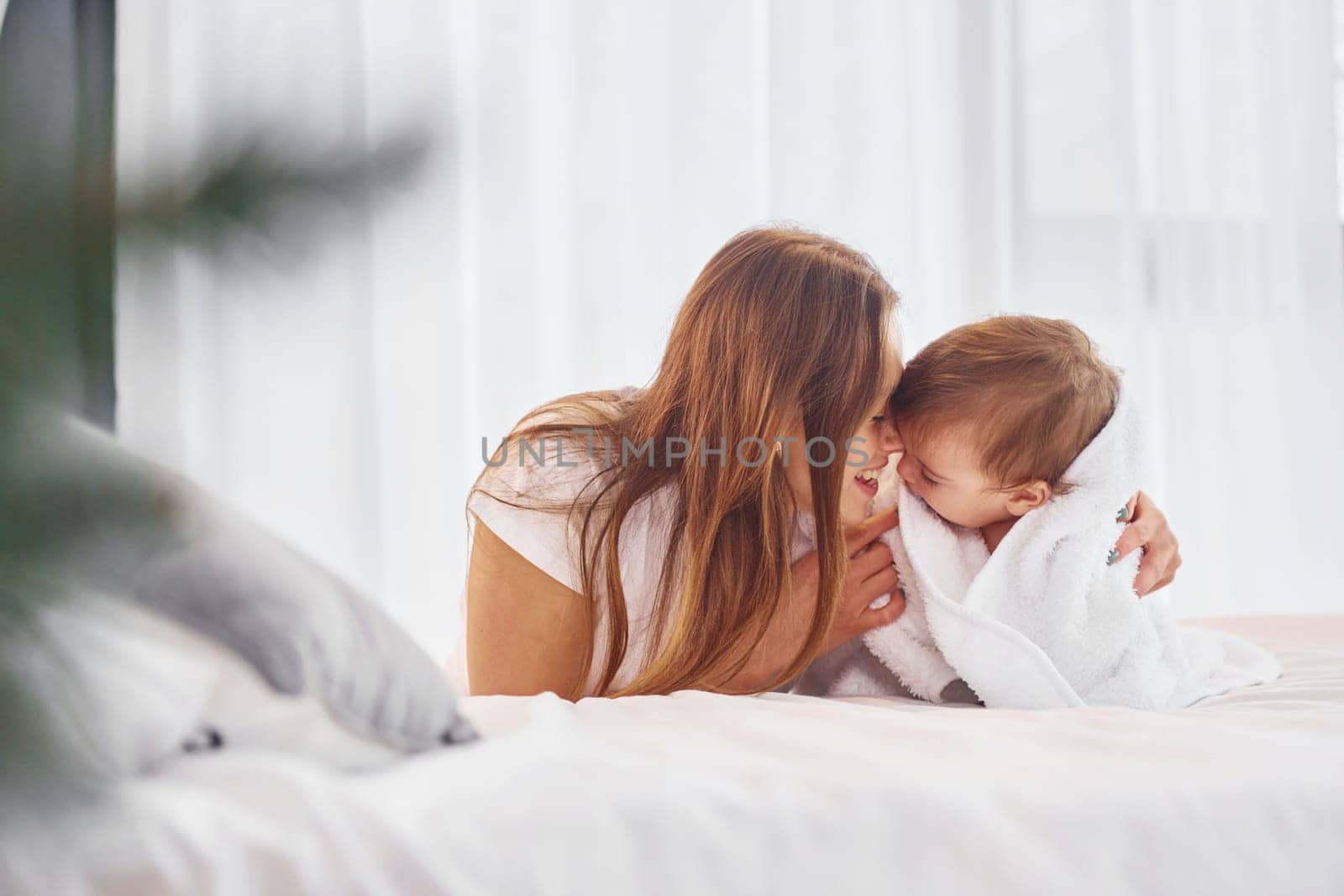 Laying down on the bed. Mother with her little daughter is indoors at home together.