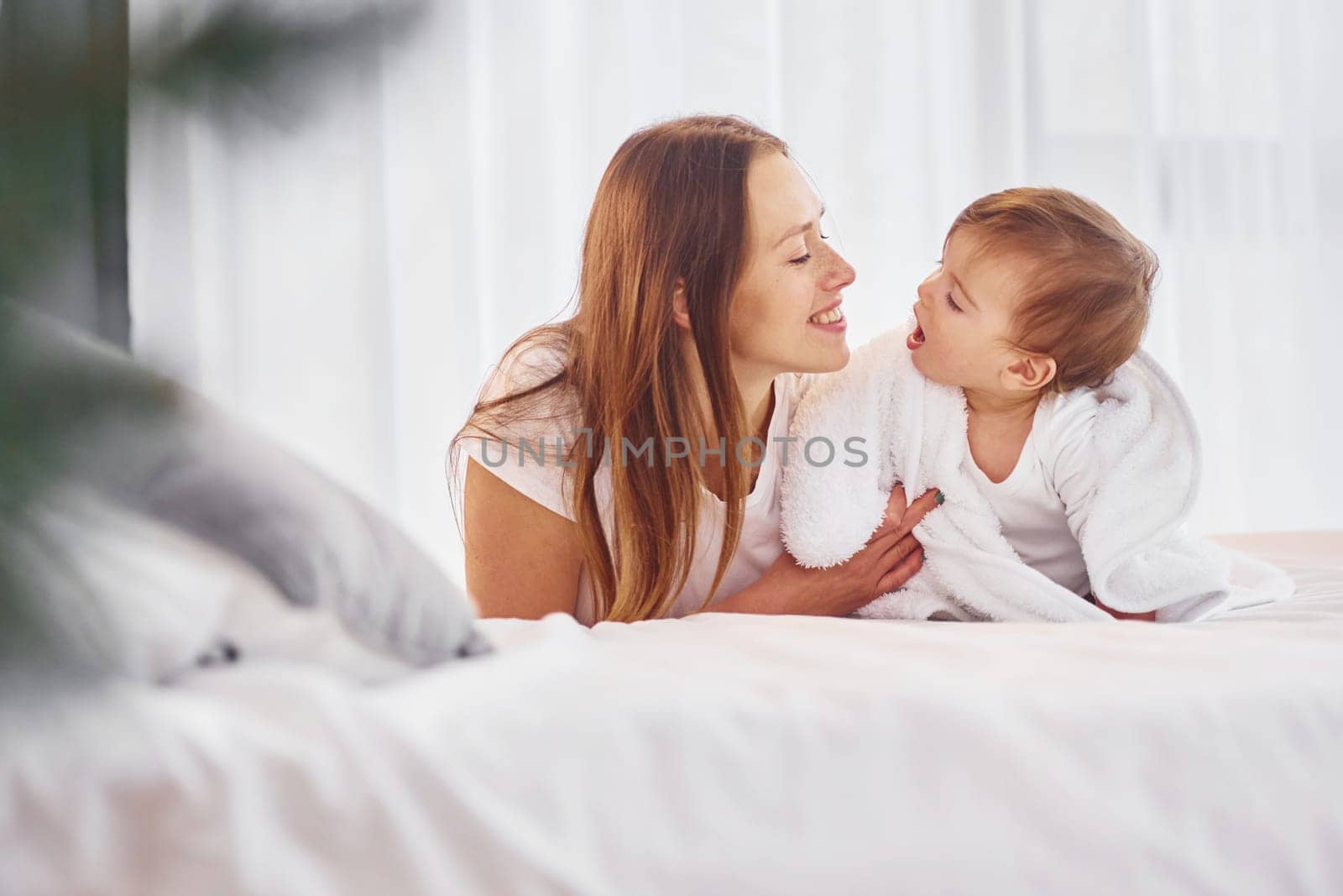 Laying down on the bed. Mother with her little daughter is indoors at home together.