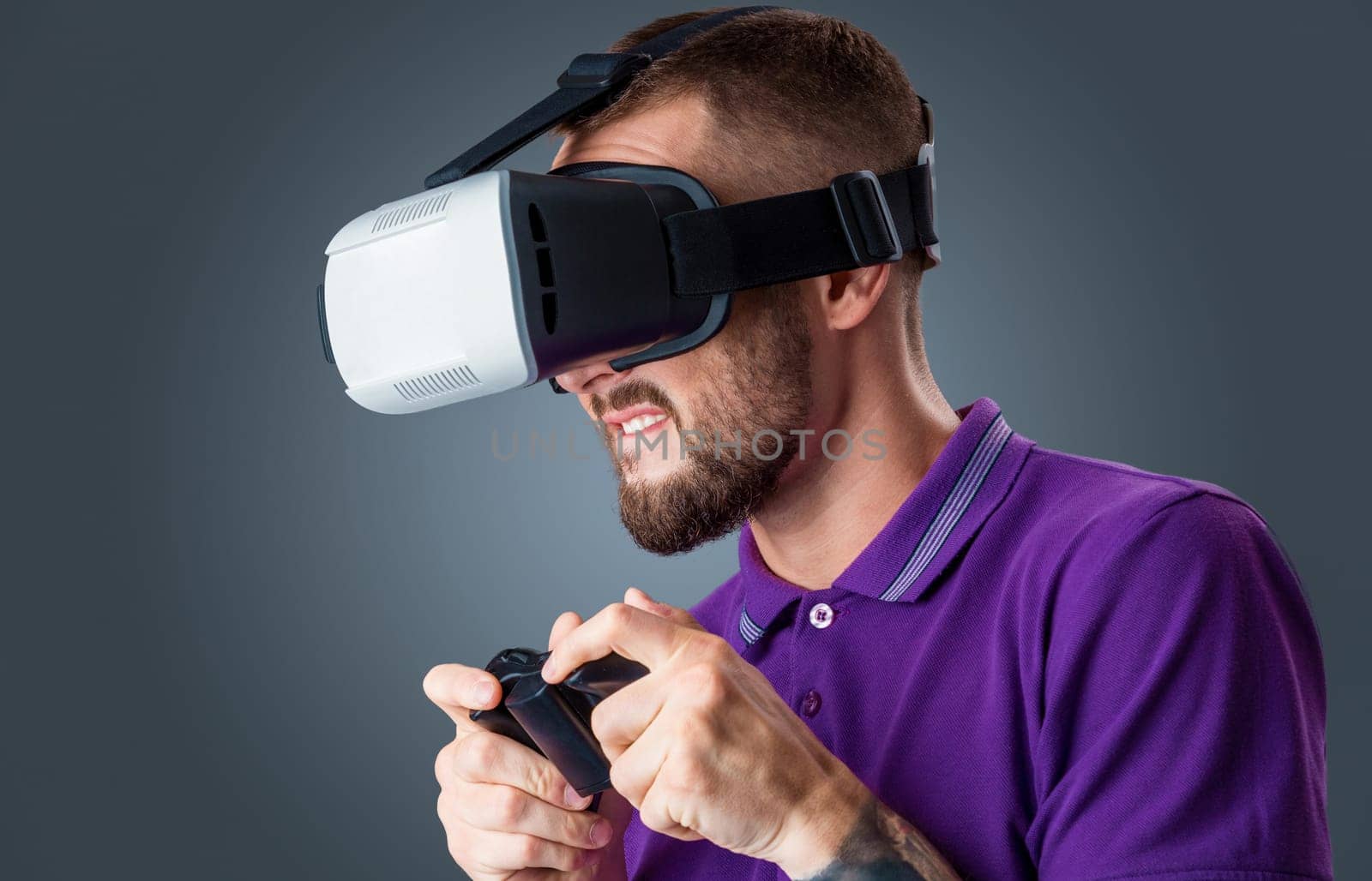 Excited young man using a VR headset glasses and experiencing virtual reality on grey blue background. with a joystick in their hands
