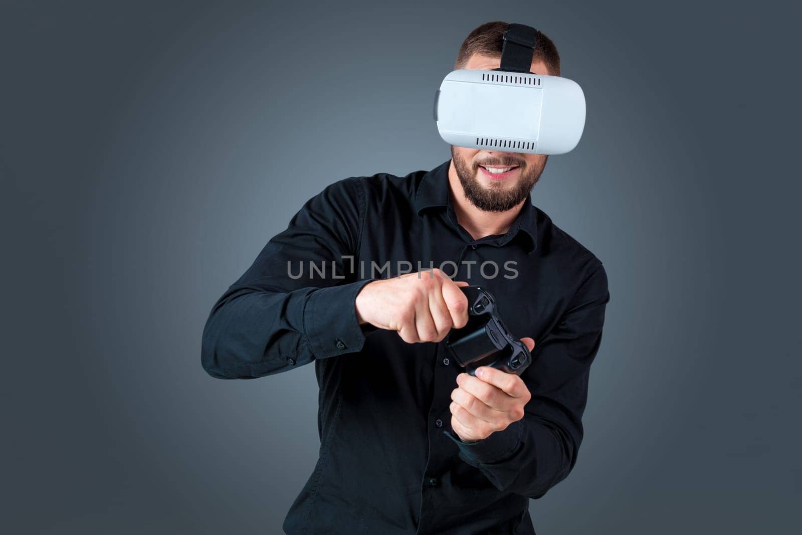 Excited young man using a VR headset glasses and experiencing virtual reality on grey blue background. with a joystick in their hands