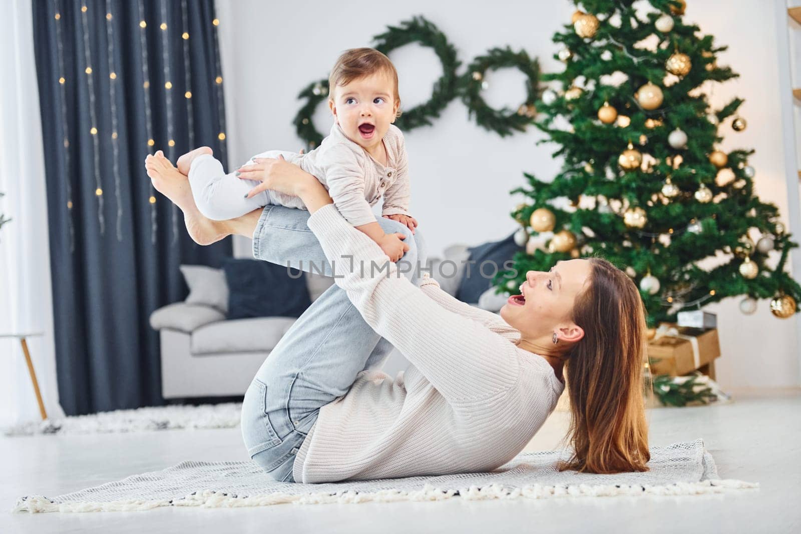 Laying down on the ground and having fun. Mother with her little daughter is indoors at home together.