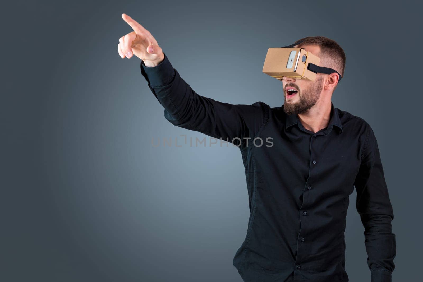 Excited young man using a VR headset glasses and experiencing virtual reality on grey blue background