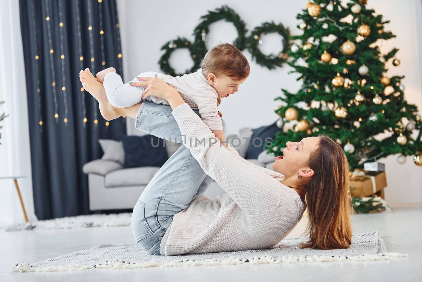 Laying down on the ground and having fun. Mother with her little daughter is indoors at home together.