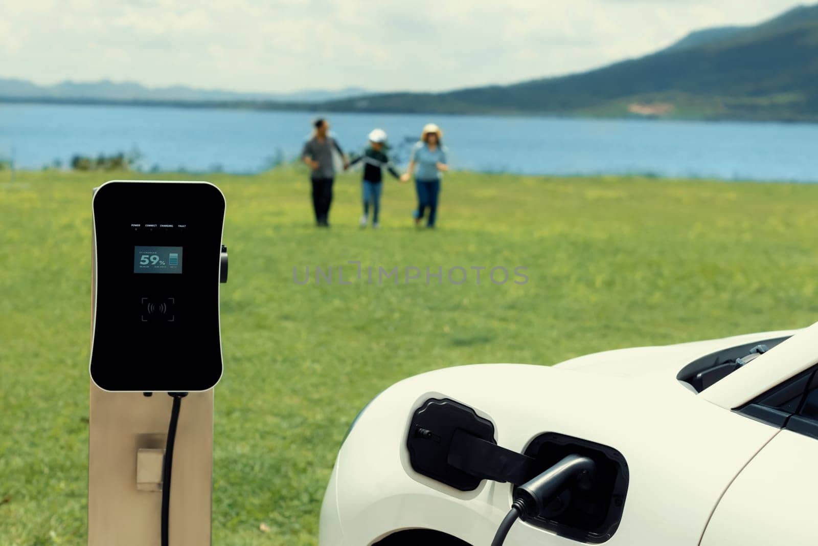 Concept of progressive happy family enjoying their time at green field and lake with electric vehicle. Electric vehicle driven by clean renewable from eco-friendly power sauce.