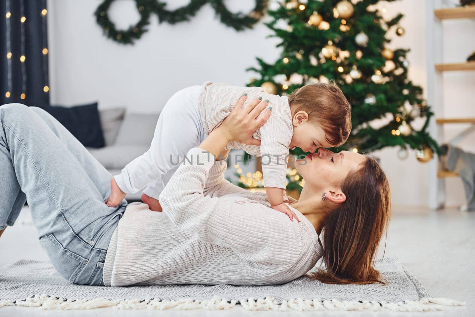 Laying down on the ground and having fun. Mother with her little daughter is indoors at home together.