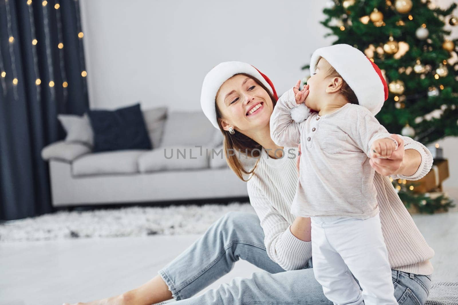 With beautiful tree. Mother with her little daughter is indoors at home together.