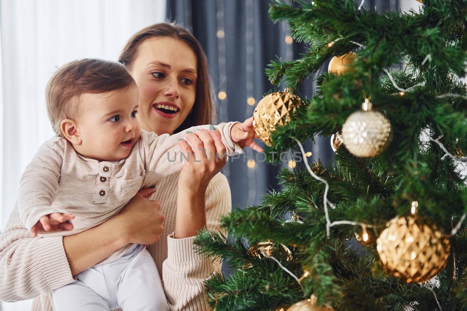 Decorating Christmas tree. Mother with her little daughter is indoors at home together.