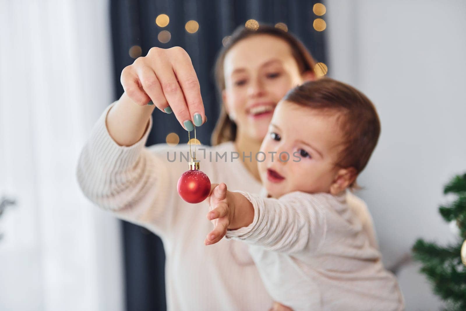 With beautiful tree. Mother with her little daughter is indoors at home together.