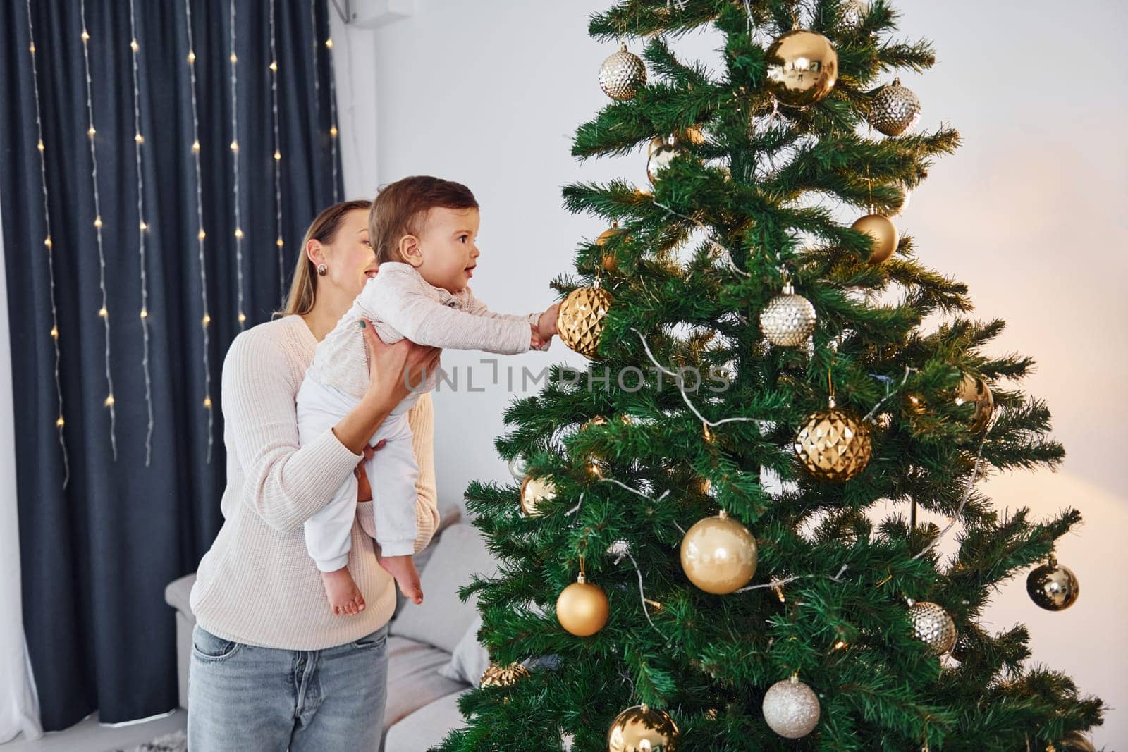 With beautiful tree. Mother with her little daughter is indoors at home together.