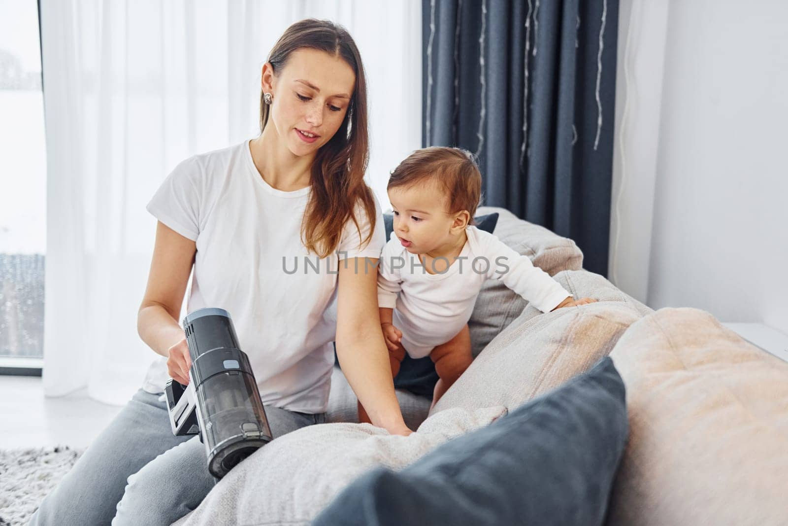Little part of the vacuum cleaner. Mother with her little daughter is indoors at home together.