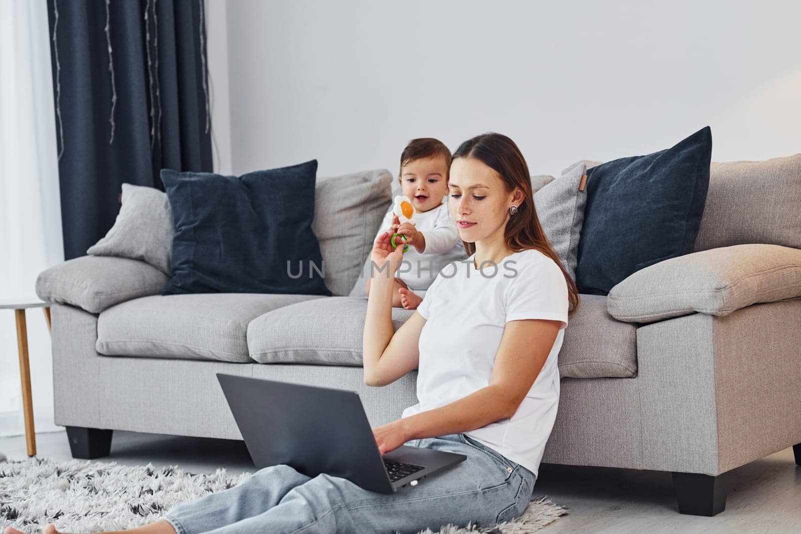 Using laptop. Mother with her little daughter is indoors at home together.