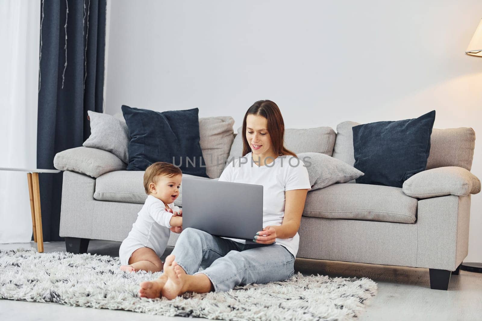 Using laptop. Mother with her little daughter is indoors at home together.