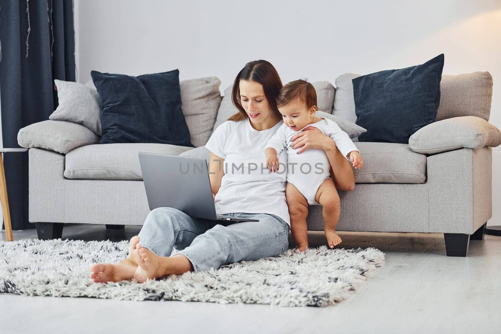 Silver colored laptop. Mother with her little daughter is indoors at home together.