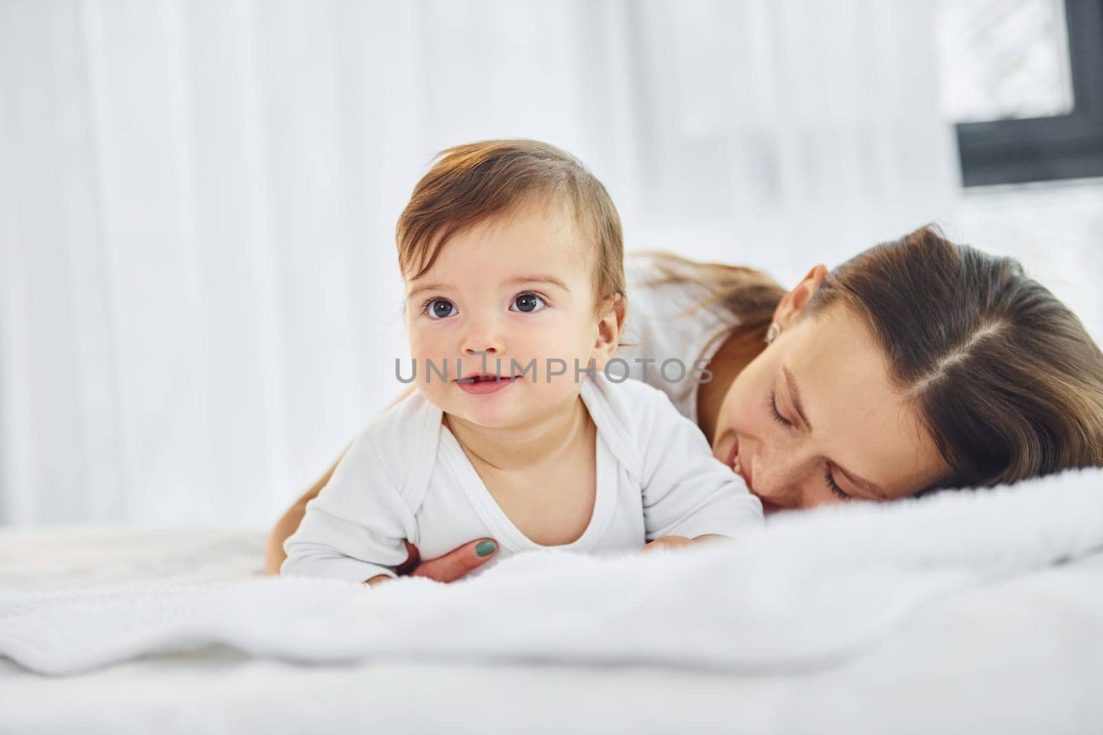 On the white bed. Mother with her little daughter is indoors at home together.