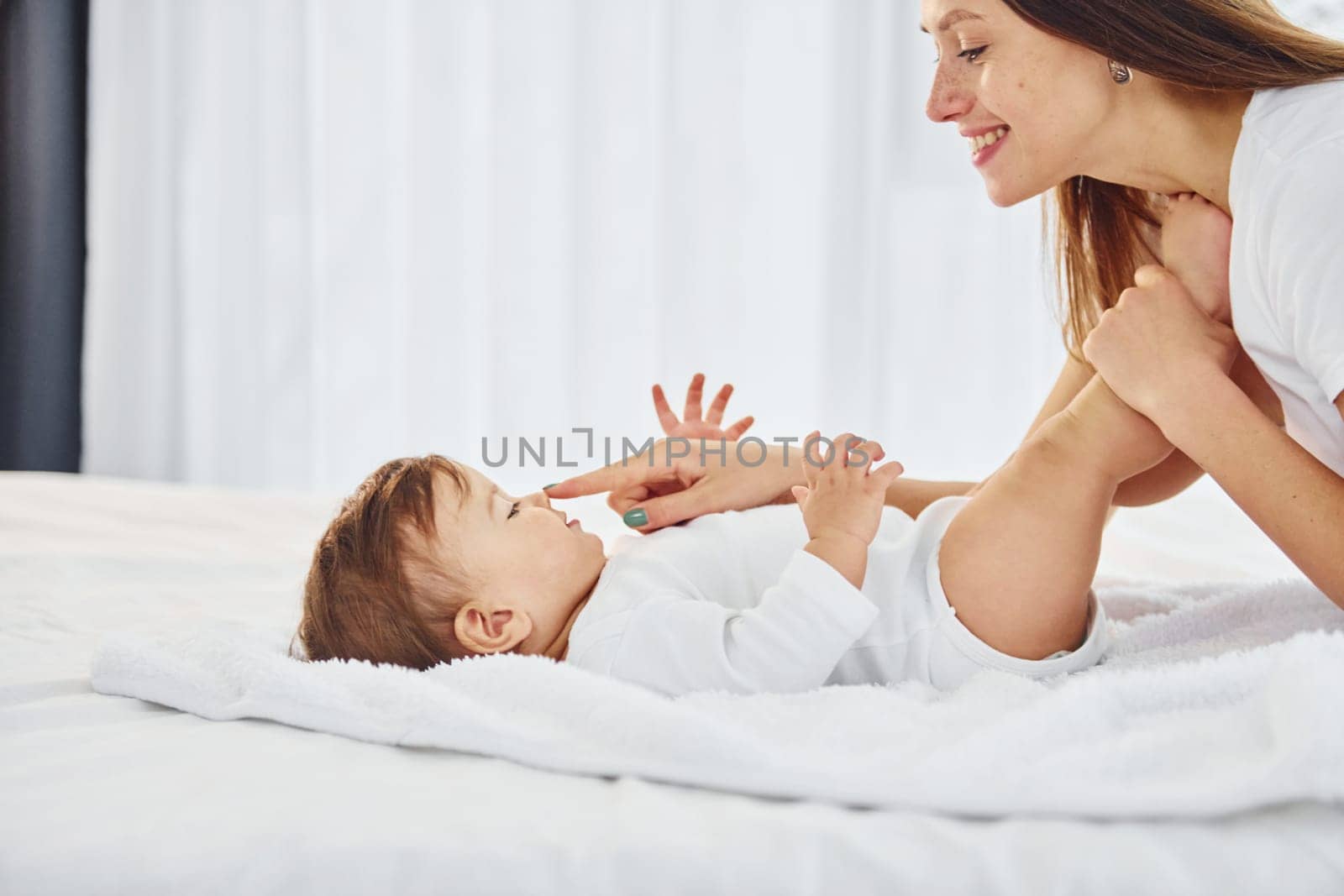 On the white bed. Mother with her little daughter is indoors at home together.