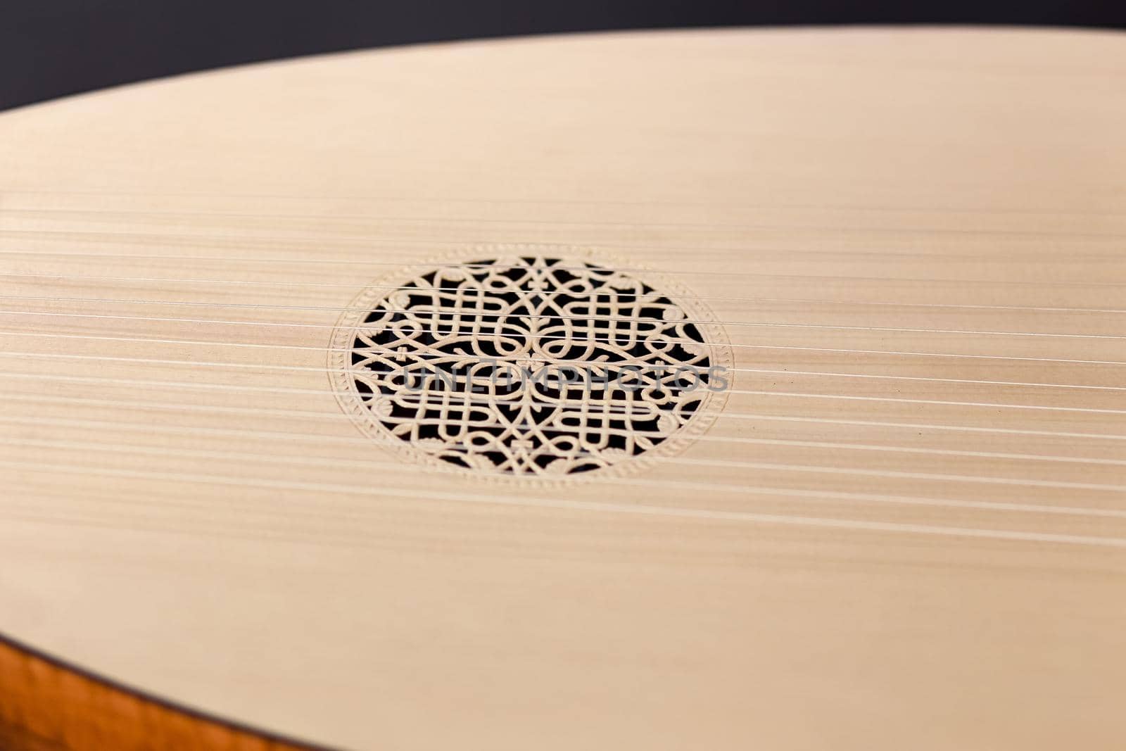 Close-up of the soundboard with the carved resonator of the lute instrument. In the middle there is a beautiful pattern in a circle. Stretched strings along the entire piece.