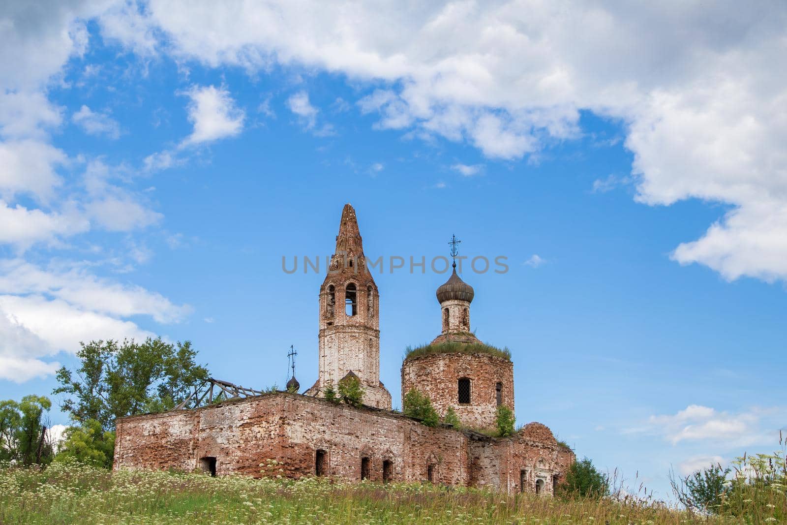 Antique destroyed cherkov against the blue sky. The red brick temple stands on a hill covered with green grass. Warm summer day.