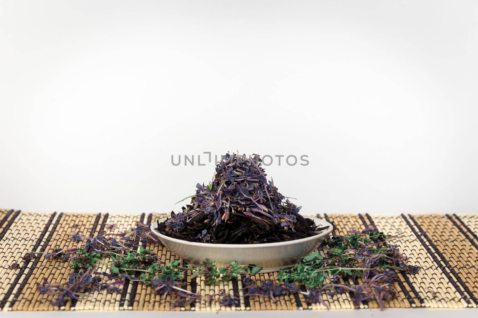 Black tea with herbs and flower leaves. A pile lies on a white plate on a bamboo stand. The isolated image on a white background.