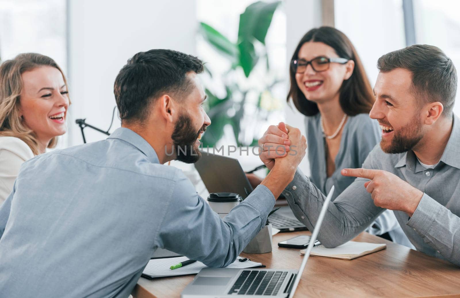 Playing arm wrestling. Group of business people that working on the project in the office.