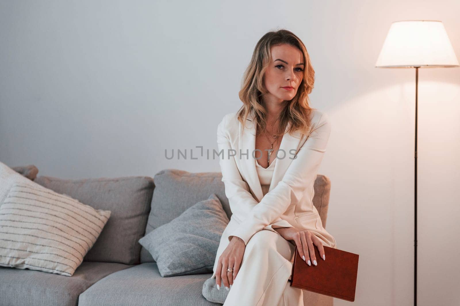 Sitting on the sofa. Business woman in formal clothes is indoors posing for the camera.