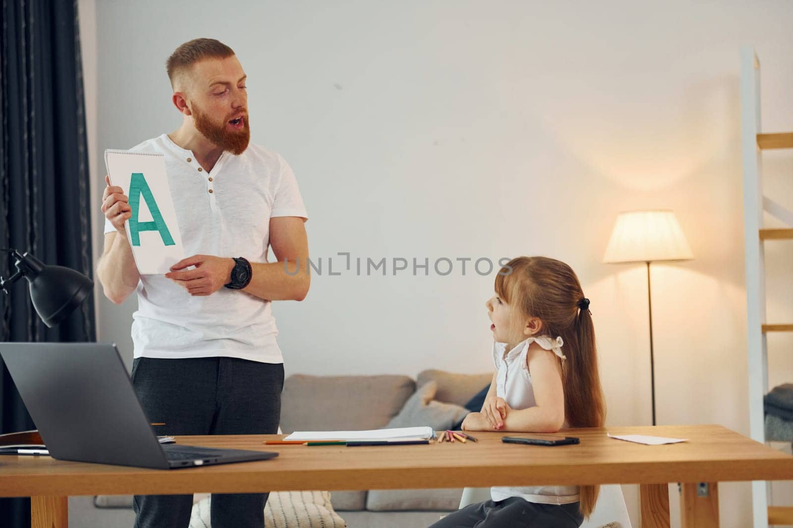 Little girl sitting by the table. Father with his little daughter is at home together.