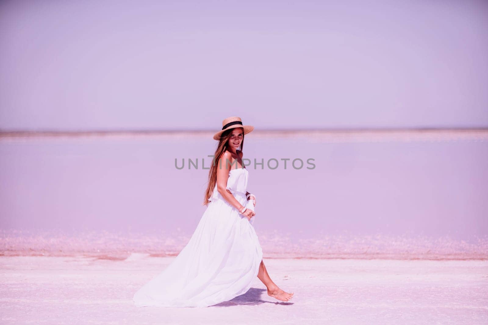 Woman in pink salt lake. She walks in a white long dress and hat along the salty white shore of the lake. Wanderlust photo for memory by Matiunina