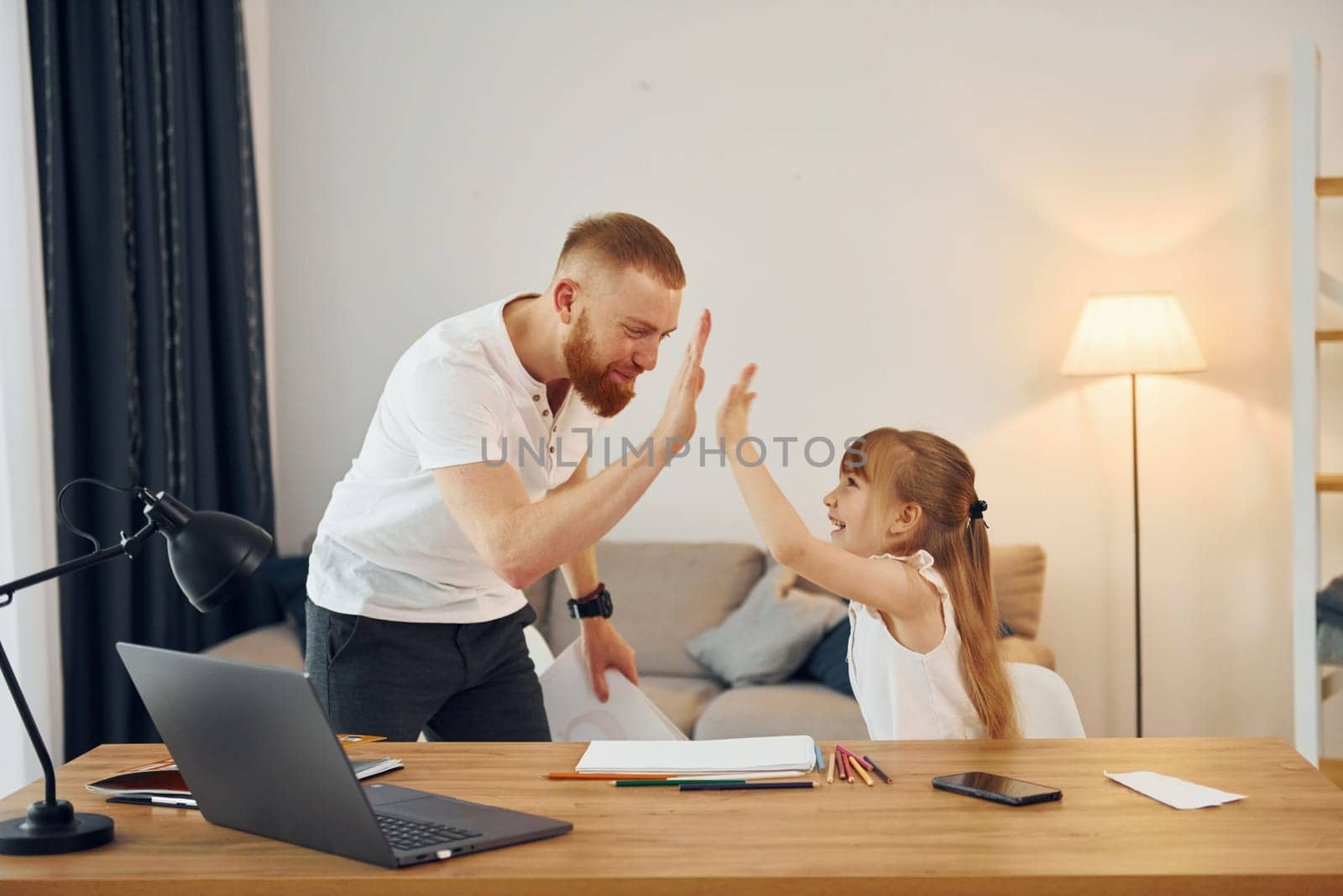 Little girl sitting by the table. Father with his little daughter is at home together.