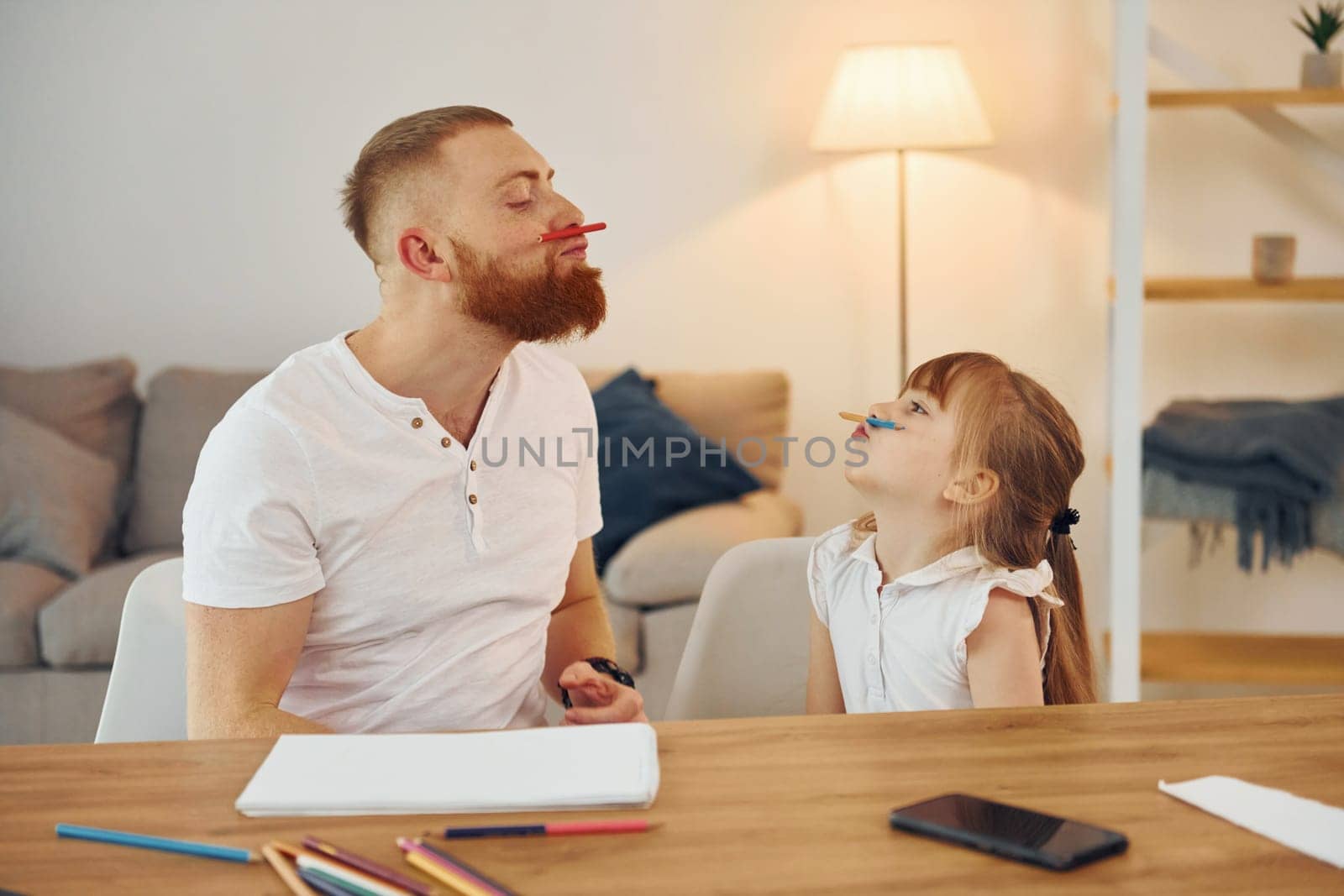 Little girl sitting by the table. Father with his little daughter is at home together.